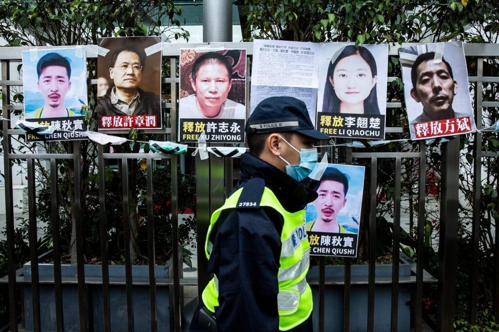 TOPSHOT - A police officer walks past placards of detained rights activists taped on the fence of the Chinese liaison office in Hong Kong on February 19, 2020, in protest against Beijings detention of prominent anti-corruption activist Xu Zhiyong. - Police in China have arrested Xu Zhiyong, a prominent anti-corruption activist who had been criticising President Xi Jinpings handling of the COVID-19 coronavirus. (Photo by ISAAC LAWRENCE / AFP) (Photo by ISAAC LAWRENCE/AFP via Getty Images)