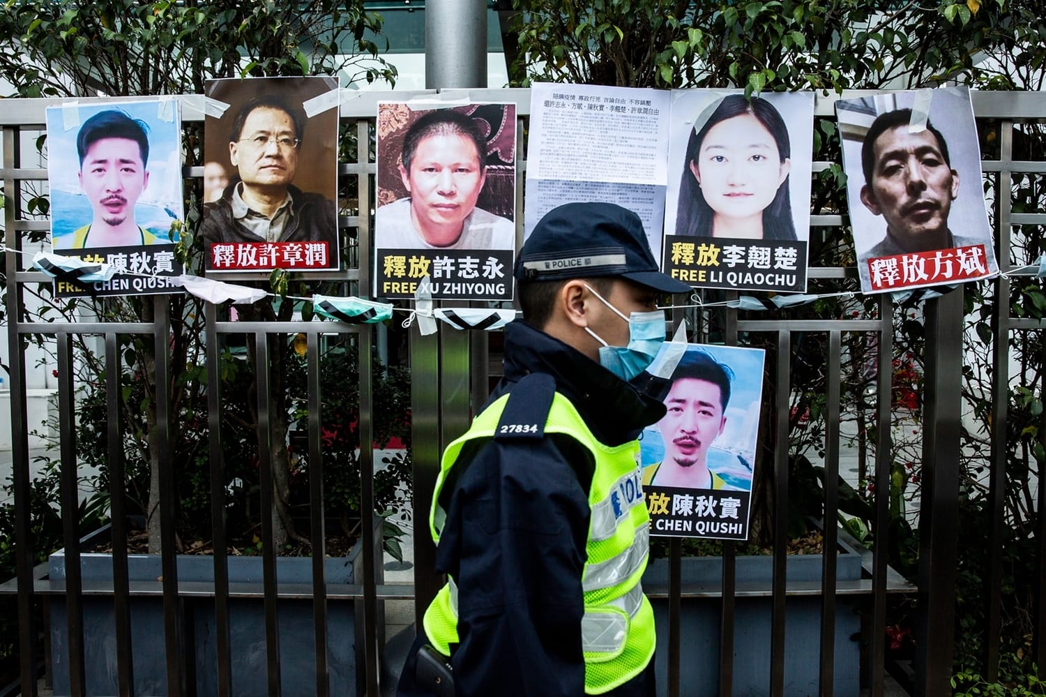 TOPSHOT - A police officer walks past placards of detained rights activists taped on the fence of the Chinese liaison office in Hong Kong on February 19, 2020, in protest against Beijings detention of prominent anti-corruption activist Xu Zhiyong. - Police in China have arrested Xu Zhiyong, a prominent anti-corruption activist who had been criticising President Xi Jinpings handling of the COVID-19 coronavirus. (Photo by ISAAC LAWRENCE / AFP) (Photo by ISAAC LAWRENCE/AFP via Getty Images)